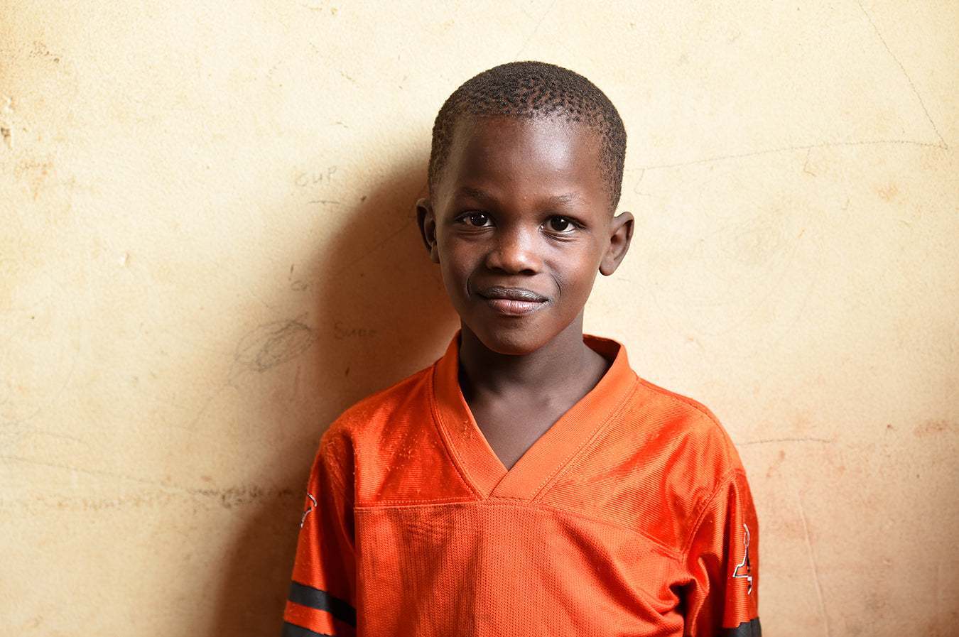 Smiling Ugandan boy in orange football jersey